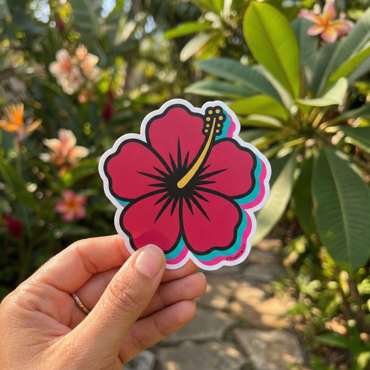 Hand holding a colorful Flor de Maga flower sticker with a garden background. Teal, hot pink, red, and golden colors are part of the national Puerto Rico Flower.