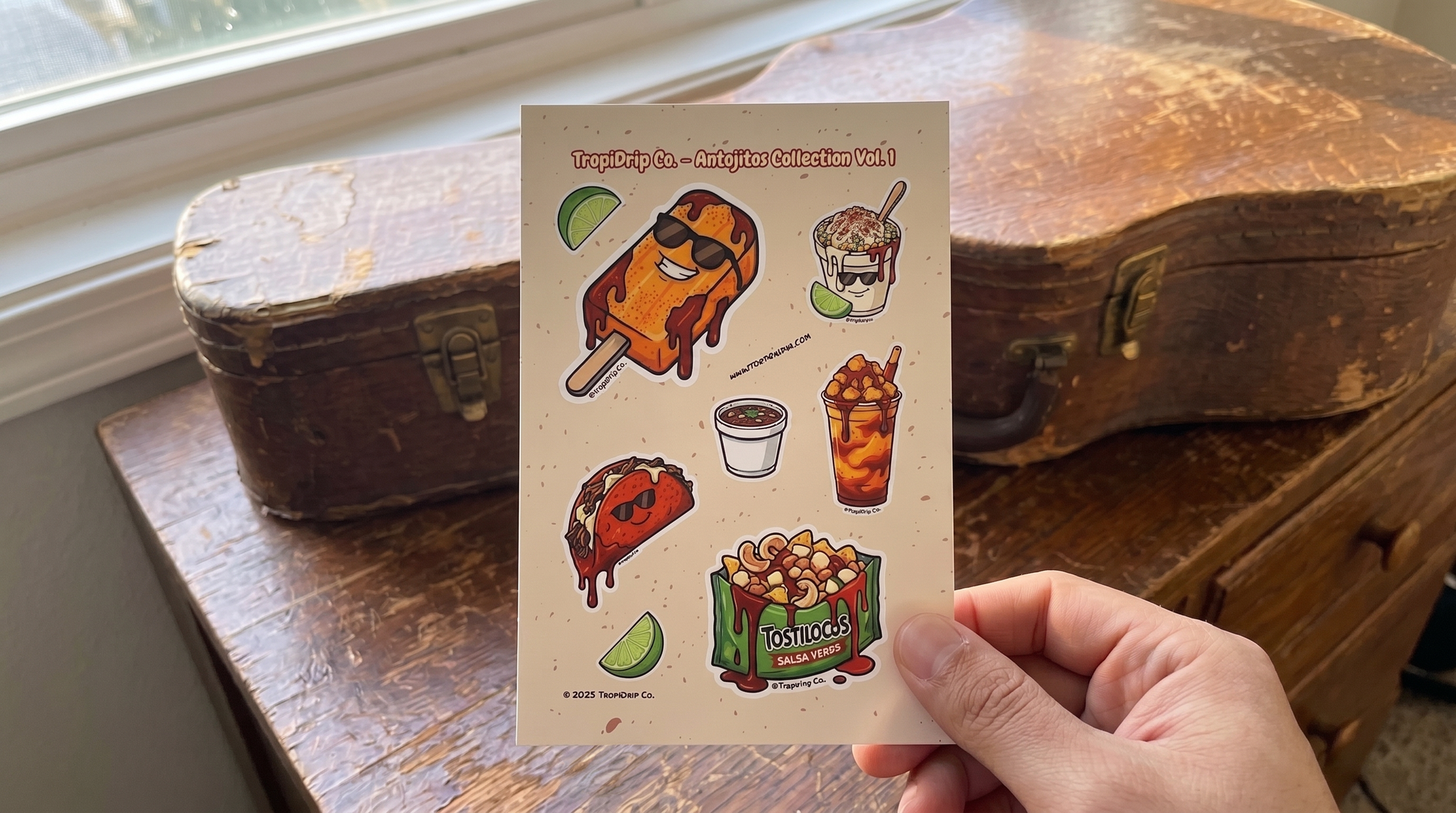 Hand holding a card with mexican food illustrations in front of an old guitar case.