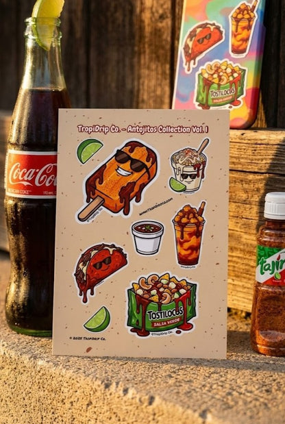 TropiDrip Co. Mexican Antojitos Sticker Sheet Vol. 1 featuring Chibi-style vinyl stickers of Tostilocos, Esquites, and Mango Paletas. The sheet is displayed outdoors in warm sunlight on a wooden surface with a tropical, high-quality aesthetic.